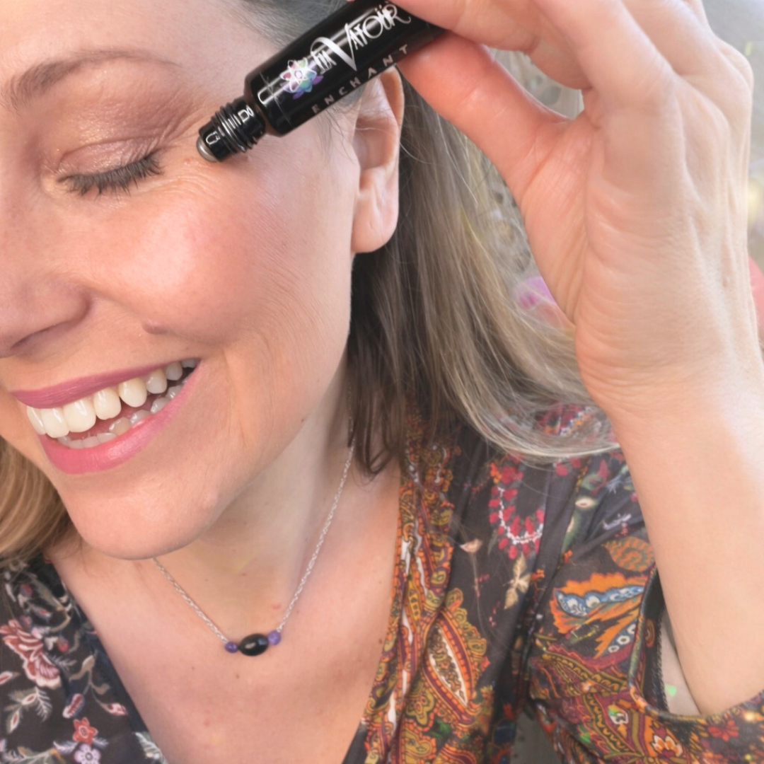 Person applying Enchant Eye Serum using the metal rollerball applicator to the orbital bone to reduce fine lines and under-eye puffiness.